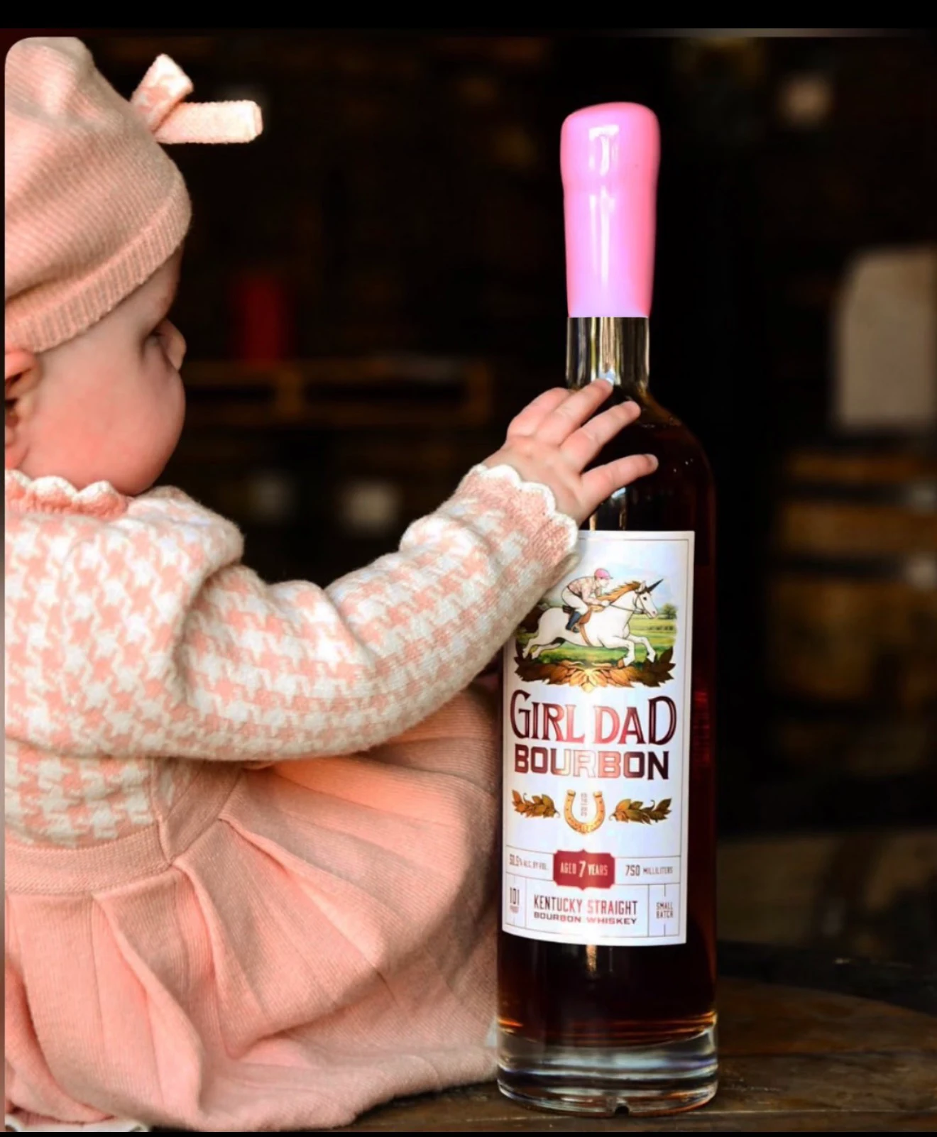 Baby beside a Girl Dad Bourbon bottle with its straight pink wax seal