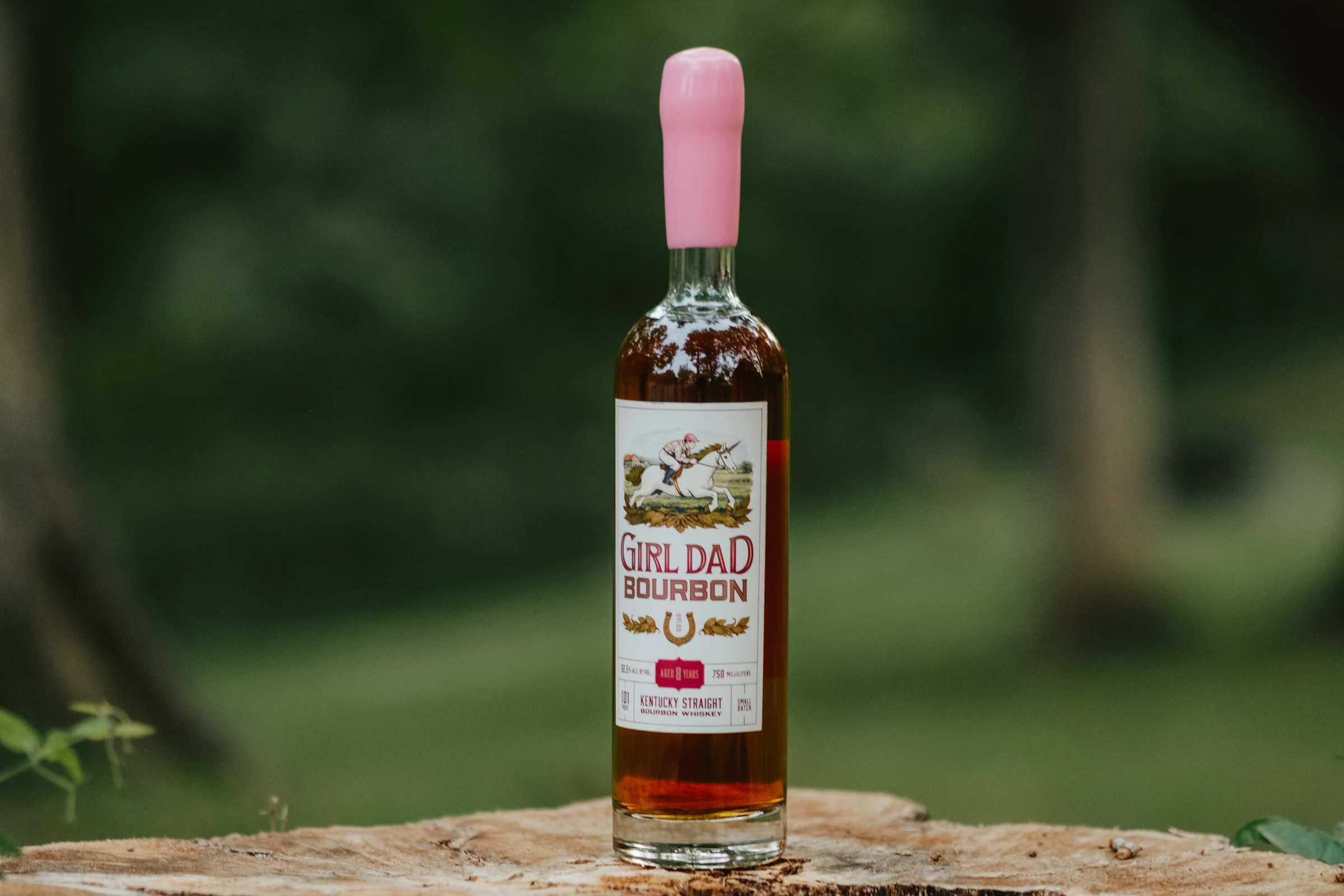 Girl Dad Bourbon 8-year bottle standing on a tree stump in a wooded setting