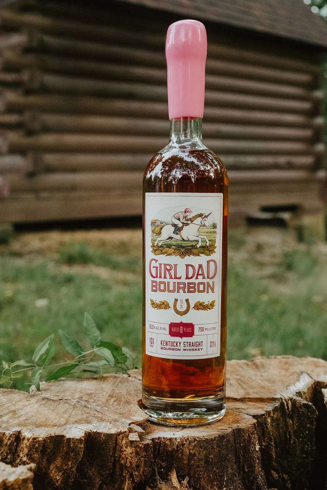 Girl Dad Bourbon 8-year bottle on a tree stump in front of a log cabin